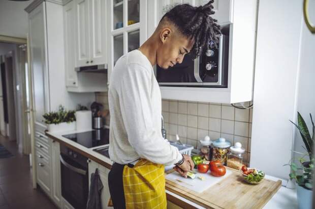 A young man chopping vegetables in his kitchen.