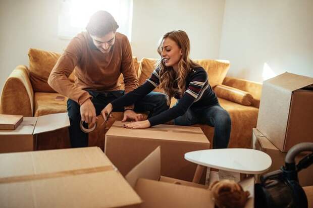 A man and woman sitting on the couch in their living room and packing up moving boxes.