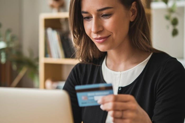 Woman holds credit cards in front of her while she uses laptop.