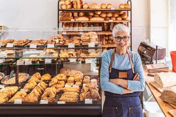 A smiling person wearing an apron in a bakery.