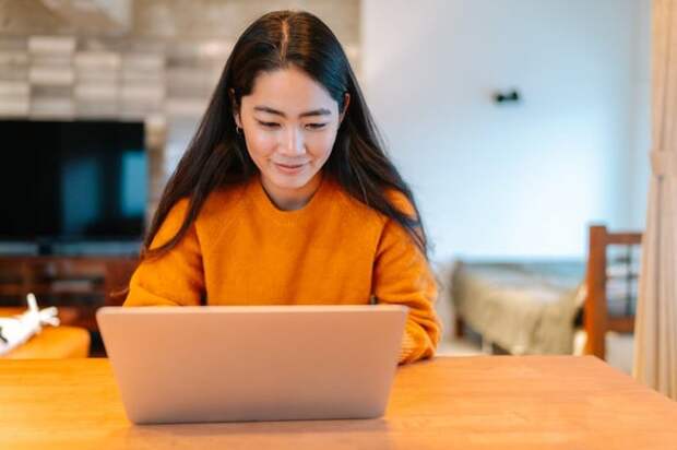 A young woman sits at home, looking at her laptop.
