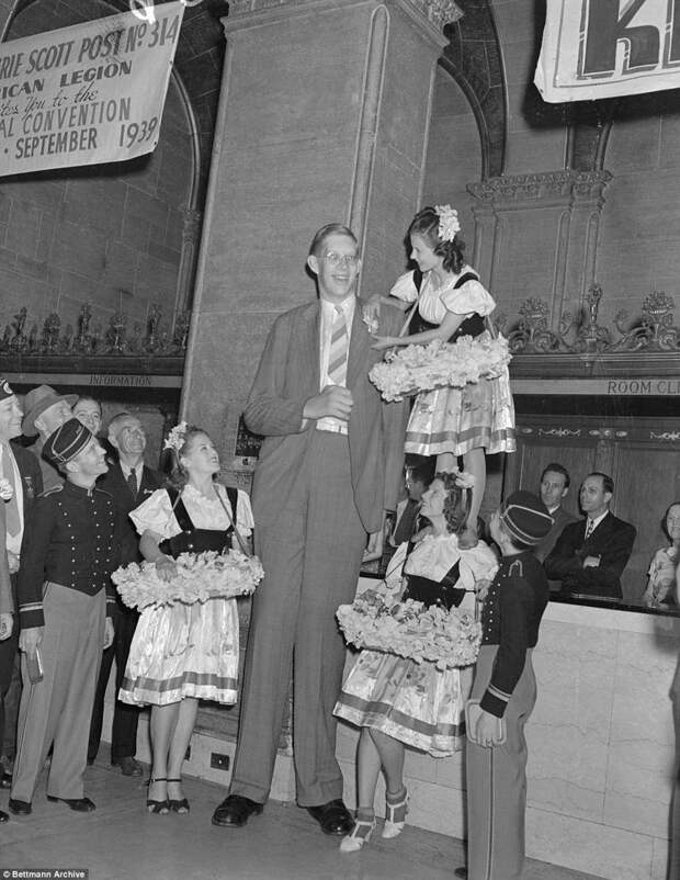 Девушки проявляют спортивную подготовку и смекалку, чтобы прикрепить цветок на лацкан пиджака Роберта акромегалия, великан, опухоль, рекорд, рекорд гиннесса, рекордсмен Гинесса, самый высокий, самый высокий человек
