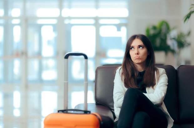 Disappointed woman sitting in airport chair next to her luggage.