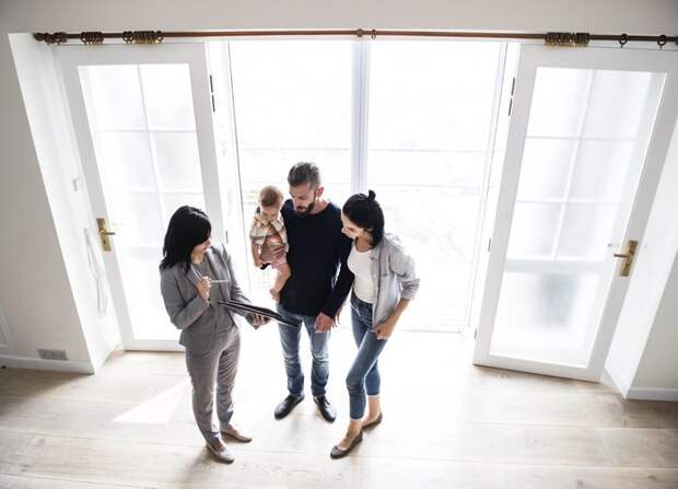 A real estate agent shows a couple with an infant a house.