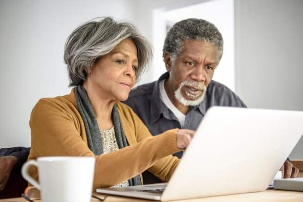 A couple looking at a laptop while seated at a table.