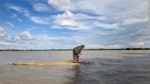 Пострадавшая от наводнения женщина на плоту приближается к лодке, ища сухое укрытие, Бангладеш. животные, климат, природа
