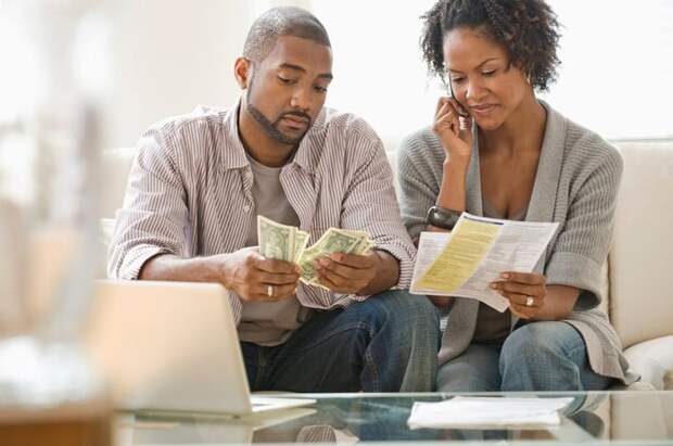 A couple pays bills on the phone and with cash at home.