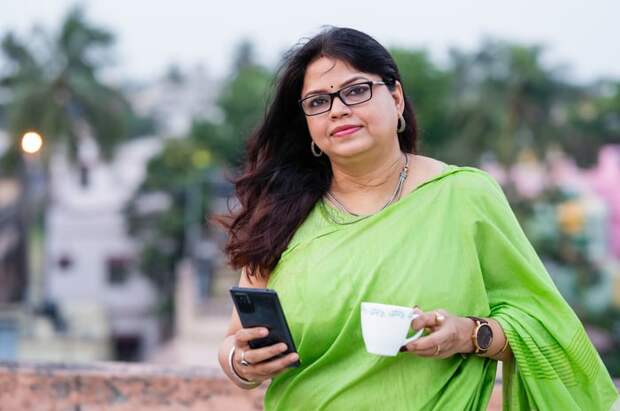 Someone looking at the camera holding a phone in one hand and a cup in their other hand.