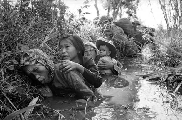 Вьетнамские женщины и дети прячутся от артиллерийского огня в заросшем канале в 30 км к западу от Сайгона, 1 января 1966 года.