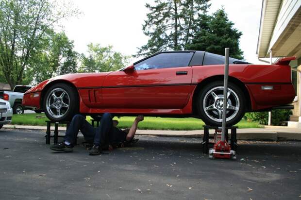 Слесарь ремонтирует Chevrolet Corvette, стоящий на стойках Lift Stand.