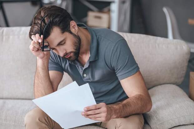 A tired-looking man resting his forehead on his hand while reading paperwork.