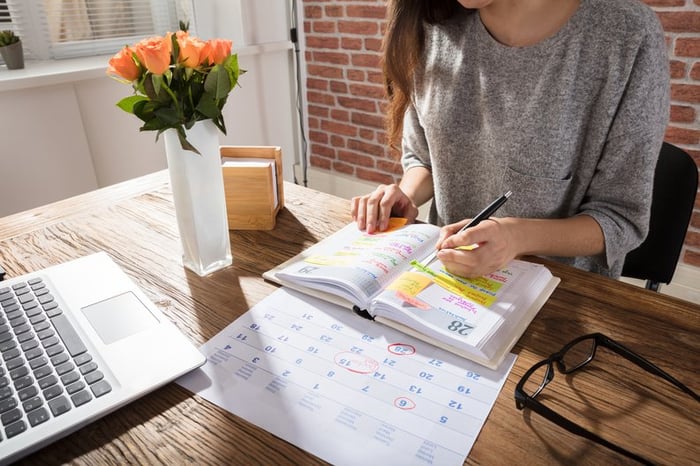 A women sitting at a sunny desk with a laptop, calendar, and planner.