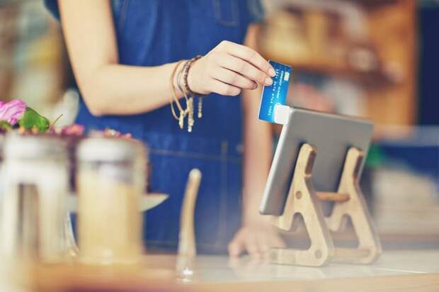 A female cashier at a restaurant swiping a credit card in a mobile card reader attached to a tablet.
