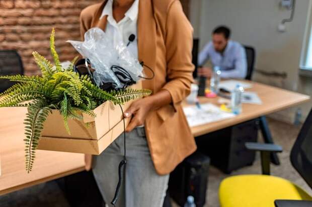 A woman walking out of an office with a cardboard box of her things after being laid off.