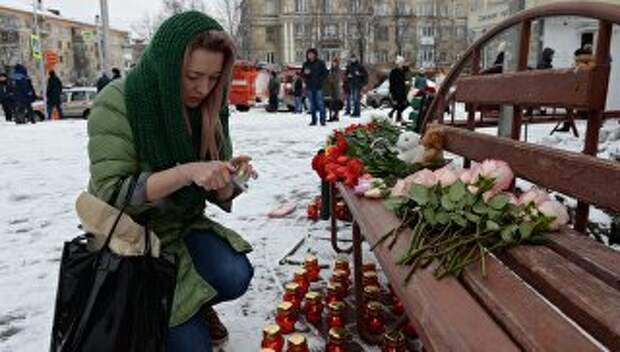 Женщина зажигает свечу возле здания торгового центра «Зимняя вишня» в Кемерово, где произошел пожар