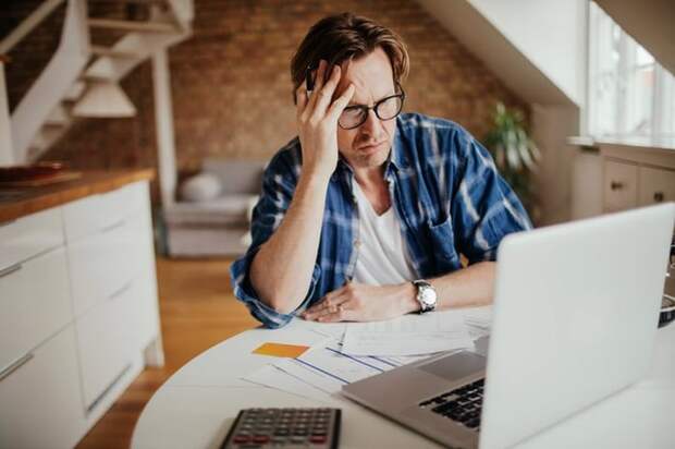 A person looks concerned at their financial documents and laptop.