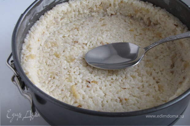 Разъемную форму диаметром 20 см смазать сливочным маслом, присыпать манкой или мукой. Выложить рис, формируя бортики при помощи ложки.