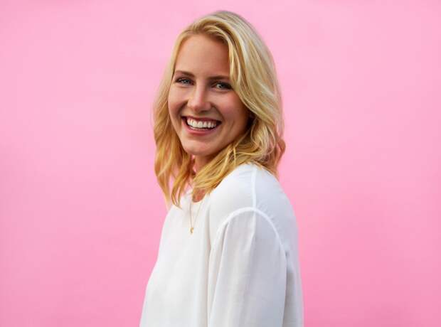 A blonde woman in a white shirt against a pink background