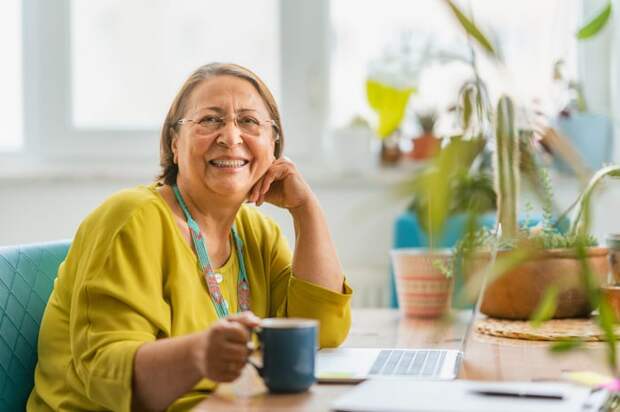 Someone is seated at a table, smiling and holding a mug.