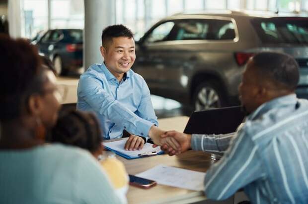 Salesman and customer shaking hands over paperwork at car dealership