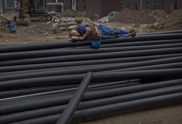 Китайский строитель спит на трубах на строительной площадке нового жилого комплекса в Пекине, Китай