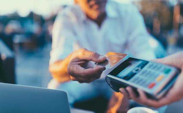 A man holding his credit card over a card payment reader.