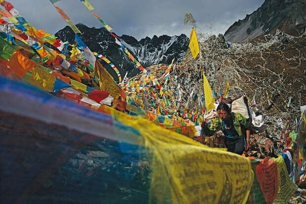 A Buddhist pilgrim climbs to sacred Mount Kawagebo in Yunnan, China, between rows of prayer flags. Her journey to circle the mountain will take nearly two weeks.