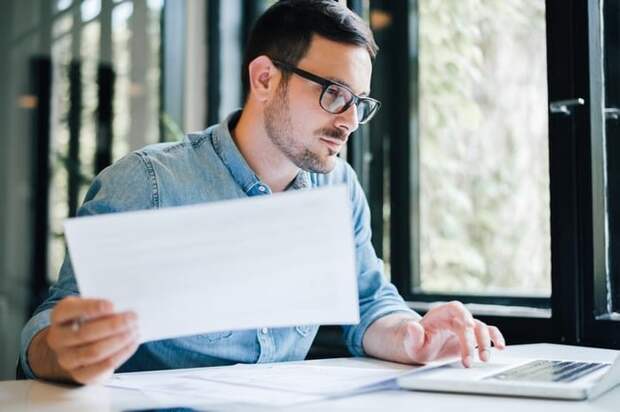 Man at desk holding document in one hand and typing with the other.